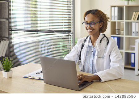 Smiling Female Doctor Using Laptop at Desk in Modern Medical Office Healthcare Smiling Female Doctor Using Laptop at Desk in Modern Medical Office Healthcare 142888590