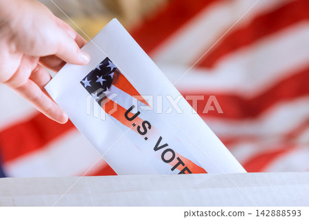 Hand places ballot into voting box with American flag behind it during an election. Hand places ballot into voting box with American flag behind it during an election. 142888593