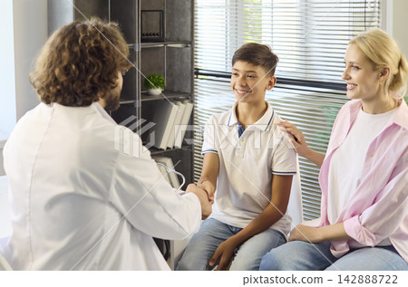 Pediatrician greeting teenage boy with handshake as supportive mother sits nearby Pediatrician greeting teenage boy with handshake as supportive mother sits nearby 142888722