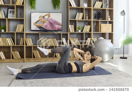 Woman doing abs workout at home, exercising with online TV fitness instruction Woman doing abs workout at home, exercising with online TV fitness instruction 142888870