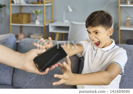 Angry boy screaming and grabbing smartphone during screen time conflict at home Angry boy screaming and grabbing smartphone during screen time conflict at home 142889090