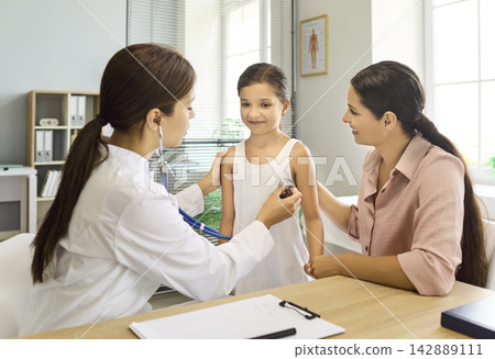 Pediatrician using stethoscope to examine child with mother during clinic visit 142889111