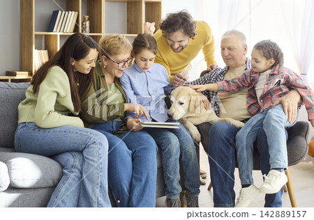 Grandparents parents and kids using a tablet together at home with dog on sofa 142889157