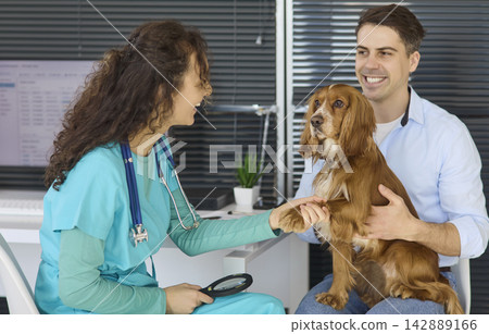Smiling veterinarian greets cocker spaniel and owner during friendly health check Smiling veterinarian greets cocker spaniel and owner during friendly health check 142889166