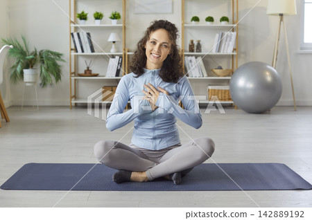 Happy sporty fit yogi woman sitting in lotus pose, cross-legged on mat, peaceful pose smiling warmly Happy sporty fit yogi woman sitting in lotus pose, cross-legged on mat, peaceful pose smiling warmly 142889192