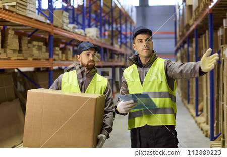 Supervisor directs warehouse worker in inventory stocktaking with clipboard, boxes Supervisor directs warehouse worker in inventory stocktaking with clipboard, boxes 142889223