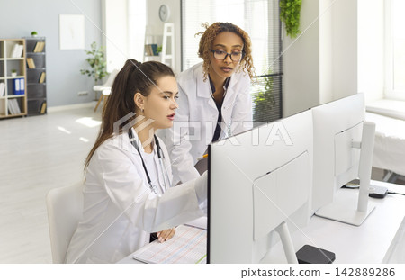 Doctors collaborating at computers reviewing patient records in clinic office Doctors collaborating at computers reviewing patient records in clinic office 142889286