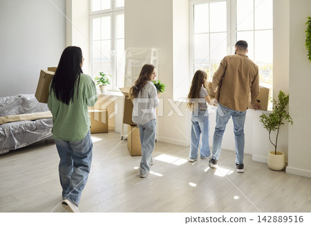 Rear view of family with children moving boxes into sunny new home, by windows Rear view of family with children moving boxes into sunny new home, by windows 142889516
