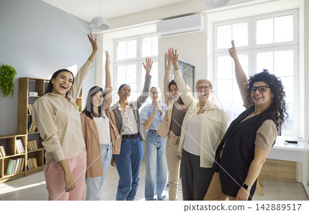 Business women cheering in office, raising hands to celebrate success and unity Business women cheering in office, raising hands to celebrate success and unity 142889517