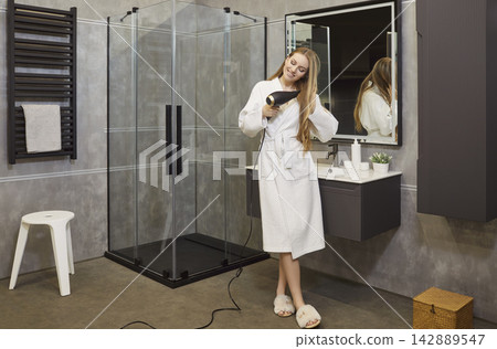 Happy smiling young girl drying hair using hairdryer in modern bathroom interior Happy smiling young girl drying hair using hairdryer in modern bathroom interior 142889547