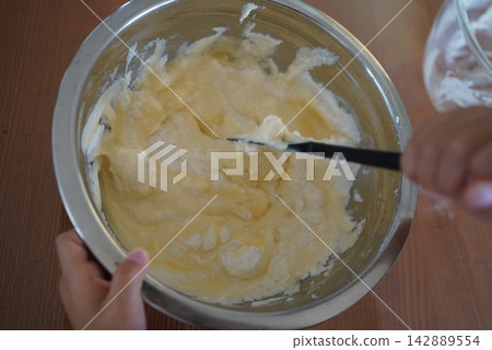 一個孩子用刮刀攪拌麵團,準備製作甜點。 一個孩子用刮刀攪拌麵團,準備製作甜點。 142889554