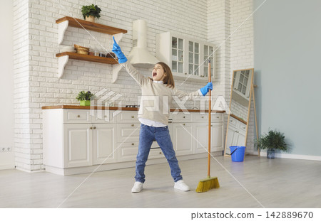 Cute funny little child wearing blue cleaning gloves holding broom in bright, modern kitchen Cute funny little child wearing blue cleaning gloves holding broom in bright, modern kitchen 142889670