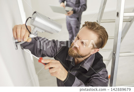 Portrait of young technician man installing surveillance CCTV camera on wall indoors Portrait of young technician man installing surveillance CCTV camera on wall indoors 142889679