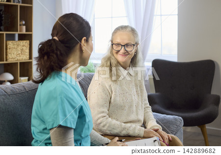 Friendly nurse discussing care plan with smiling senior woman at home visit Friendly nurse discussing care plan with smiling senior woman at home visit 142889682