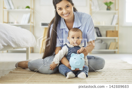 Smiling mother and baby holding a blue piggybank, savings and early money habits Smiling mother and baby holding a blue piggybank, savings and early money habits 142889683