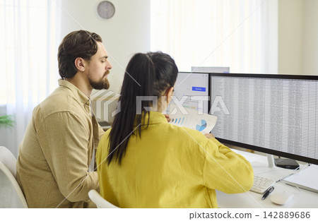 Coworkers analyzing large spreadsheets on dual monitors in bright modern office Coworkers analyzing large spreadsheets on dual monitors in bright modern office 142889686