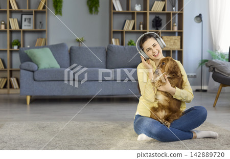 Happy woman in headphones hugging cocker spaniel at home on cozy living room floor Happy woman in headphones hugging cocker spaniel at home on cozy living room floor 142889720