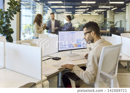 Young analyst working with financial spreadsheet at desktop in collaborative office Young analyst working with financial spreadsheet at desktop in collaborative office 142889721