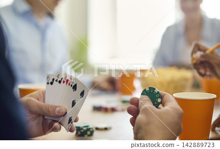 Friends playing poker, closeup of hands with cards and chips on table indoors Friends playing poker, closeup of hands with cards and chips on table indoors 142889723