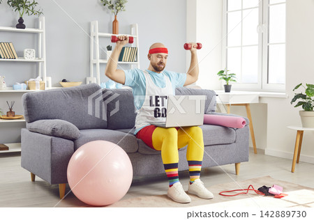 Funny Man Exercising With Dumbbells And Laptop At Home Gym Funny Man Exercising With Dumbbells And Laptop At Home Gym 142889730
