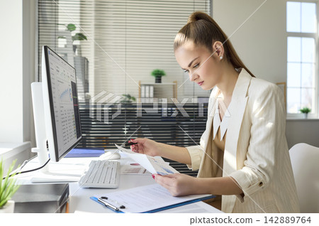 Businesswoman analyzing marketing data at desktop computer in bright modern office 142889764