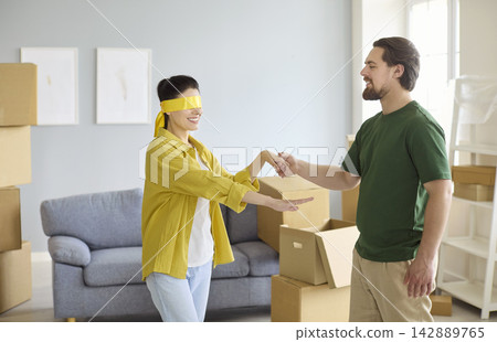 Happy couple moving into new home, man leads blindfolded woman for sweet surprise Happy couple moving into new home, man leads blindfolded woman for sweet surprise 142889765