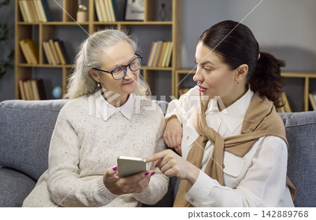 Senior woman with caregiver using smartphone at home, consultant guidance support 142889768