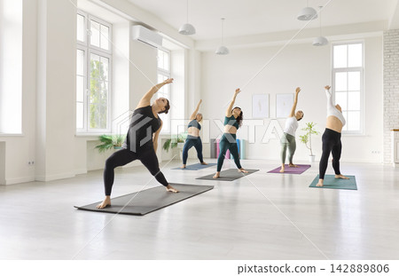 Group yoga students doing side bends in bright studio during guided fitness class Group yoga students doing side bends in bright studio during guided fitness class 142889806