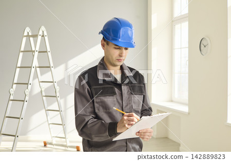 Construction worker in helmet with clipboard inspecting renovation site indoors Construction worker in helmet with clipboard inspecting renovation site indoors 142889823