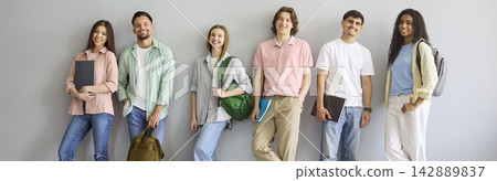 Row of university students with backpacks and books posing by blank wall Row of university students with backpacks and books posing by blank wall 142889837