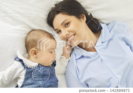 Sweet sleep of baby next to mother, top view of mom and little son lying on bed at home together Sweet sleep of baby next to mother, top view of mom and little son lying on bed at home together 142889871