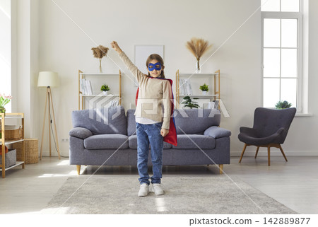 Happy boy wearing superhero costume with red cape and blue mask playing at home 142889877