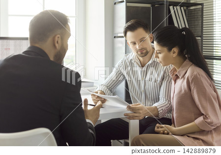 Couple reviewing paperwork with real estate agent on contract and mortgage Couple reviewing paperwork with real estate agent on contract and mortgage 142889879