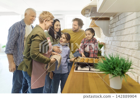 Smiling multigenerational family taking cookies from oven in bright kitchen Smiling multigenerational family taking cookies from oven in bright kitchen 142889904
