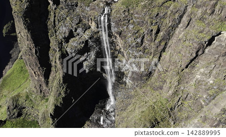 Tall narrow waterfall cascading down a rugged cliff in a remote canyon landscape . Media 142889995