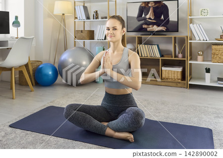 Young woman practicing yoga at home, online meditation class on television Young woman practicing yoga at home, online meditation class on television 142890002