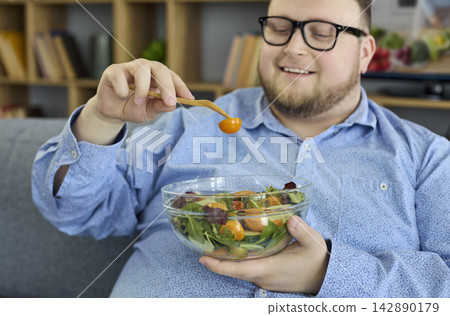 Smiling overweight man enjoying fresh salad at home for healthy diet and wellness Smiling overweight man enjoying fresh salad at home for healthy diet and wellness 142890179