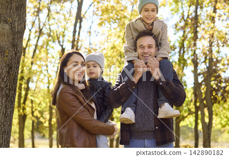 Parents with two kids smiling in sunny autumn park, boy on father's shoulders Parents with two kids smiling in sunny autumn park, boy on father's shoulders 142890182