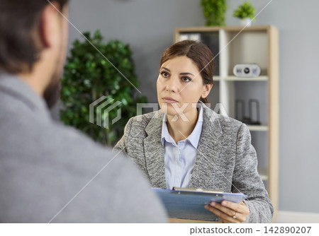 Focused HR manager listening to candidate and reviewing application documents Focused HR manager listening to candidate and reviewing application documents 142890207