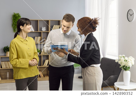 Happy Couple Reviewing Signing Rental Agreement with Professional Agent Indoors Happy Couple Reviewing Signing Rental Agreement with Professional Agent Indoors 142890352
