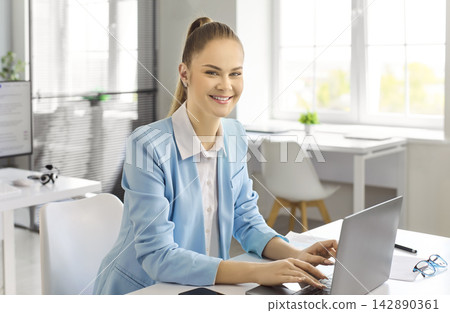 Smiling businesswoman accountant working on laptop in bright modern office interior Smiling businesswoman accountant working on laptop in bright modern office interior 142890361