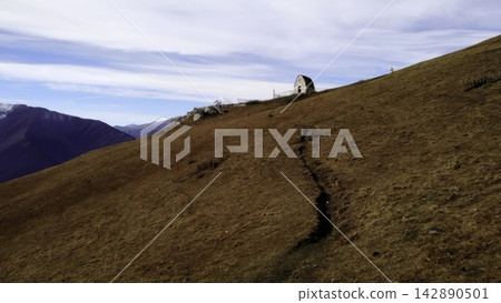 Remote mountain slope with trail and small hut Remote mountain slope with trail and small hut 142890501