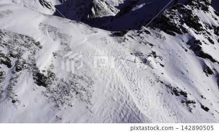 Aerial view of snowy mountain slope with rocky ridges Aerial view of snowy mountain slope with rocky ridges 142890505