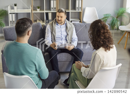 Young couple sitting back on chairs and listening to psychologist on therapy session. 142890542