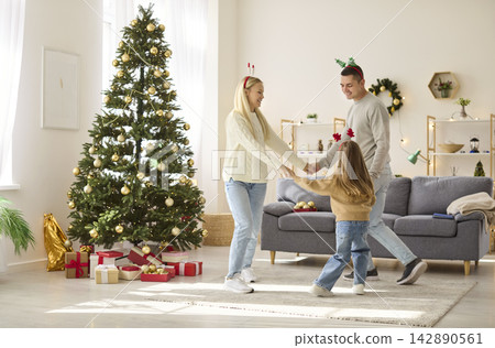 Parents and child dancing by Christmas tree in bright cozy living room home 142890561