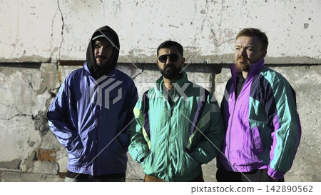 Trio Of Men Dressed In Retro Attire Standing Confidently With Gritty Urban Environment Behind Them. Media Trio Of Men Dressed In Retro Attire Standing Confidently With Gritty Urban Environment Behind Them. Media 142890562