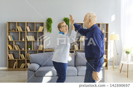 Joyful senior couple high five at home, celebrating success, love and vitality Joyful senior couple high five at home, celebrating success, love and vitality 142890697