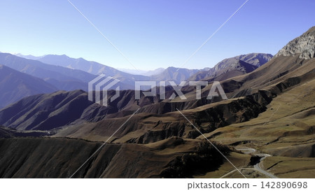 Arid mountain landscape with winding road under clear blue sky Arid mountain landscape with winding road under clear blue sky 142890698