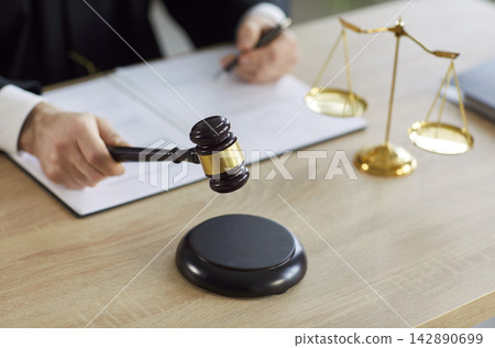 Close-up of judge holding gavel sits at table with scales of justice in courtroom Close-up of judge holding gavel sits at table with scales of justice in courtroom 142890699