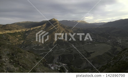 Golden Glow Highlights Winding Mountain Road. Remote Valley Houses Amid Rugged Terrain And Scenic Vistas. Creative Golden Glow Highlights Winding Mountain Road. Remote Valley Houses Amid Rugged Terrain And Scenic Vistas. Creative 142890700